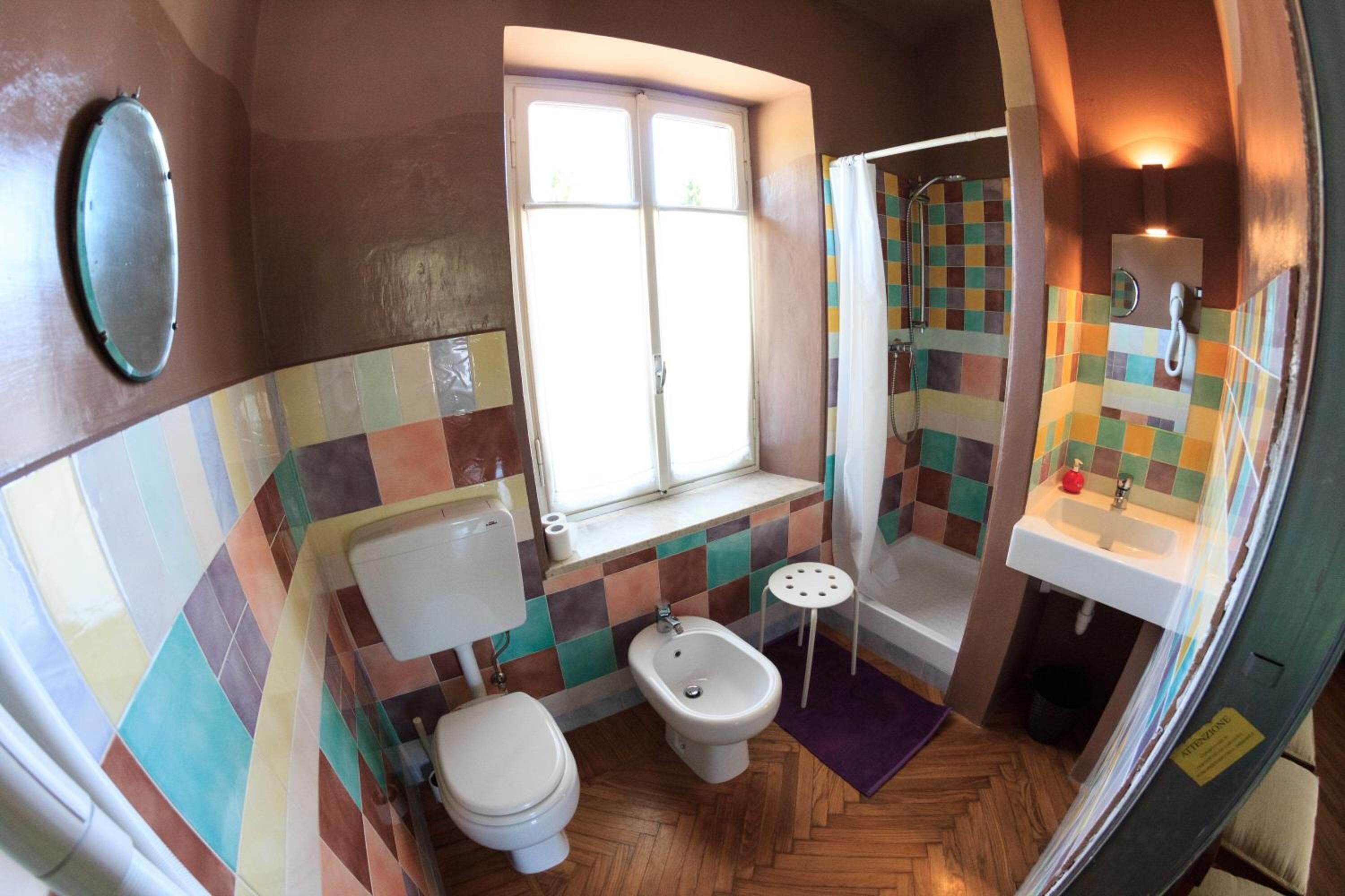 A bathroom with a toilet, bidet, and sink, featuring colorful tile walls and a herringbone floor pattern.