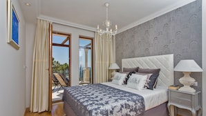 Une chambre avec un grand lit, un lustre et une vue sur l’extérieur, visible à travers une porte vitrée.