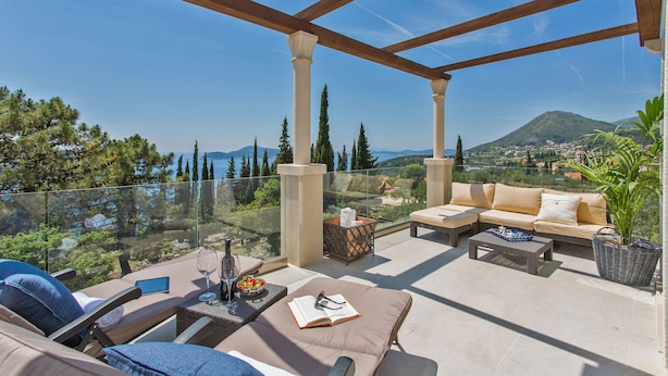 Un espace extérieur aménagé avec des sièges, baigné de lumière naturelle, doté d’une balustrade en verre, de canapés confortables et offrant une vue sur un paysage montagneux.