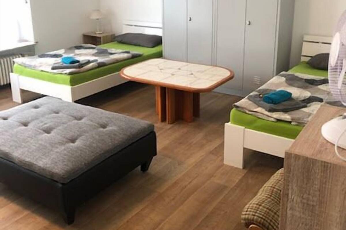 Een kleine kamer met twee eenpersoonsbedden, een tafeltje, een bankje en een kledingkast.