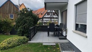 Une maison moderne dotée d’un patio couvert, d’un petit jardin et offrant une vue sur les maisons voisines.
