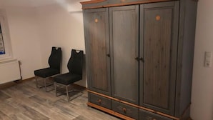 Une pièce avec une grande armoire, deux chaises noires et un radiateur.