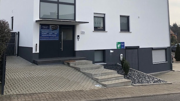 Un bâtiment moderne à deux étages, doté d’une grande baie vitrée au rez-de-chaussée, d’une enseigne indiquant un bureau de location et d’un petit espace de stationnement.