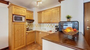 A kitchen with wooden cabinets, a microwave, a toaster, and a fruit basket on the counter. - Cozy apartment in Chamonix center with parking (Chamonix-Mont-Blanc)