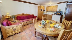 A cozy living area with a sofa, wooden side tables, and a dining table set for breakfast. - Cozy apartment in Chamonix center with parking (Chamonix-Mont-Blanc)