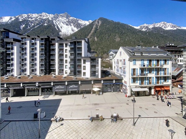 Un bâtiment moderne doté de nombreux balcons, d’une place centrale ouverte et surplombé par une chaîne de montagnes.