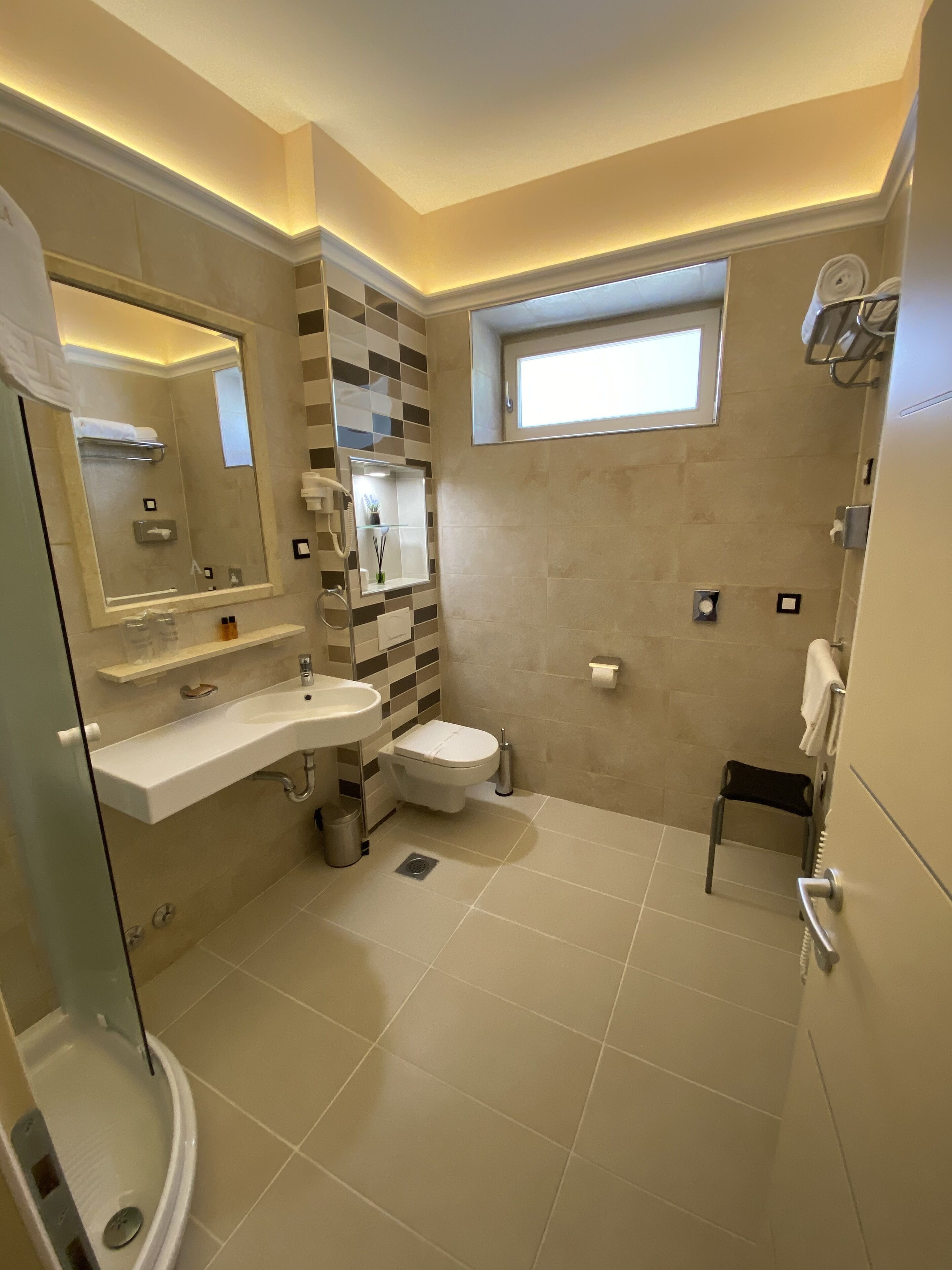Ein modernes Badezimmer mit Duschkabine aus Glas, einem Waschtisch mit Spüle und Spiegel, einer Toilette und einem Fenster für natürliches Licht.