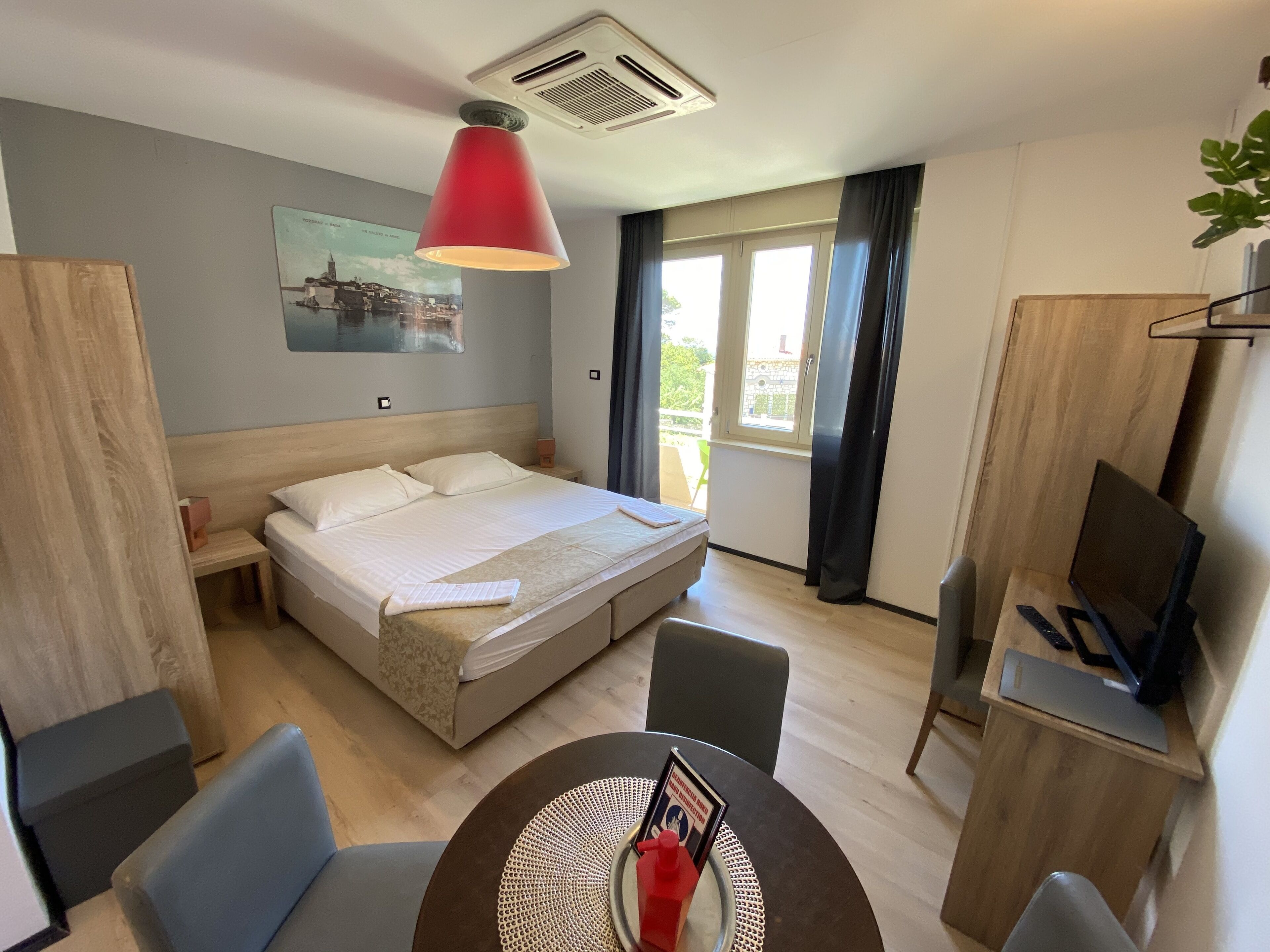 Een hotelkamer met een bed, nachtkastje, bureau, stoel en een eettafel met placemat en een boek.