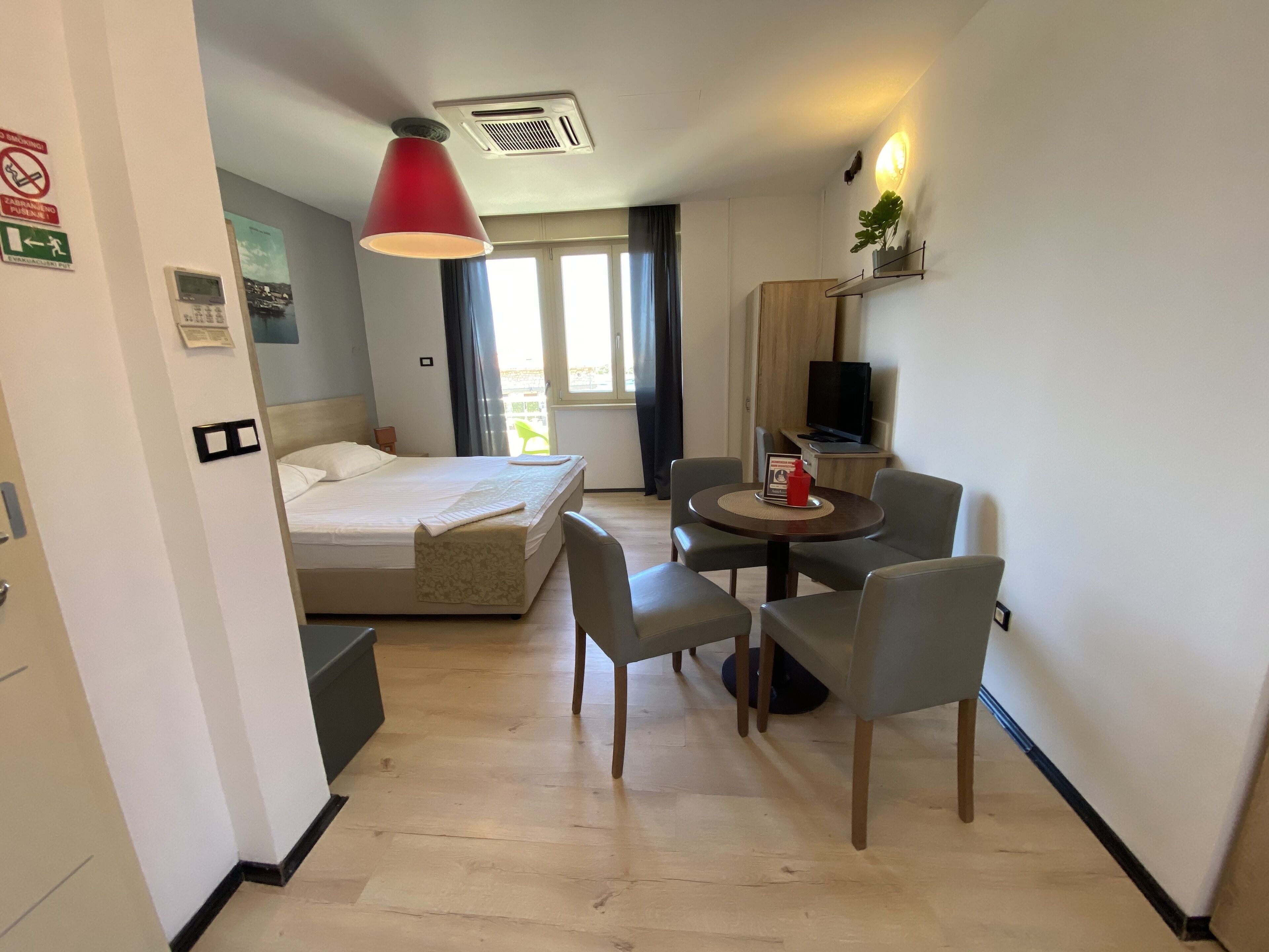 A hotel room with a bed, a desk with a chair, a television, and a window with curtains.