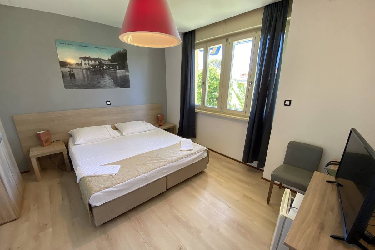 Habitación de hotel con cama, mesitas de noche, escritorio con silla, televisor y ventana con cortinas.