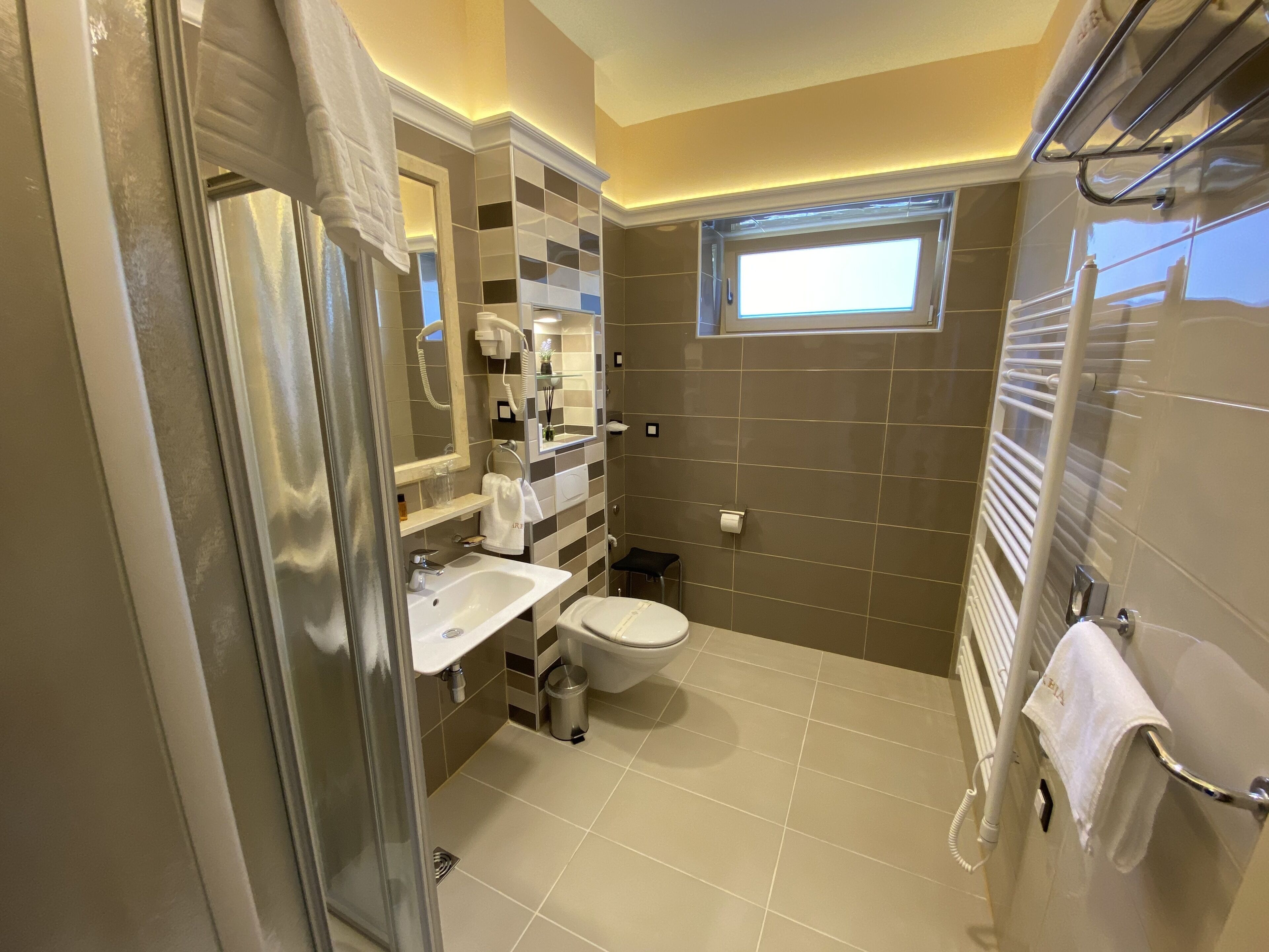 Un baño moderno con cabina de ducha de vidrio, un lavabo blanco, un inodoro y un perchero para toallas.