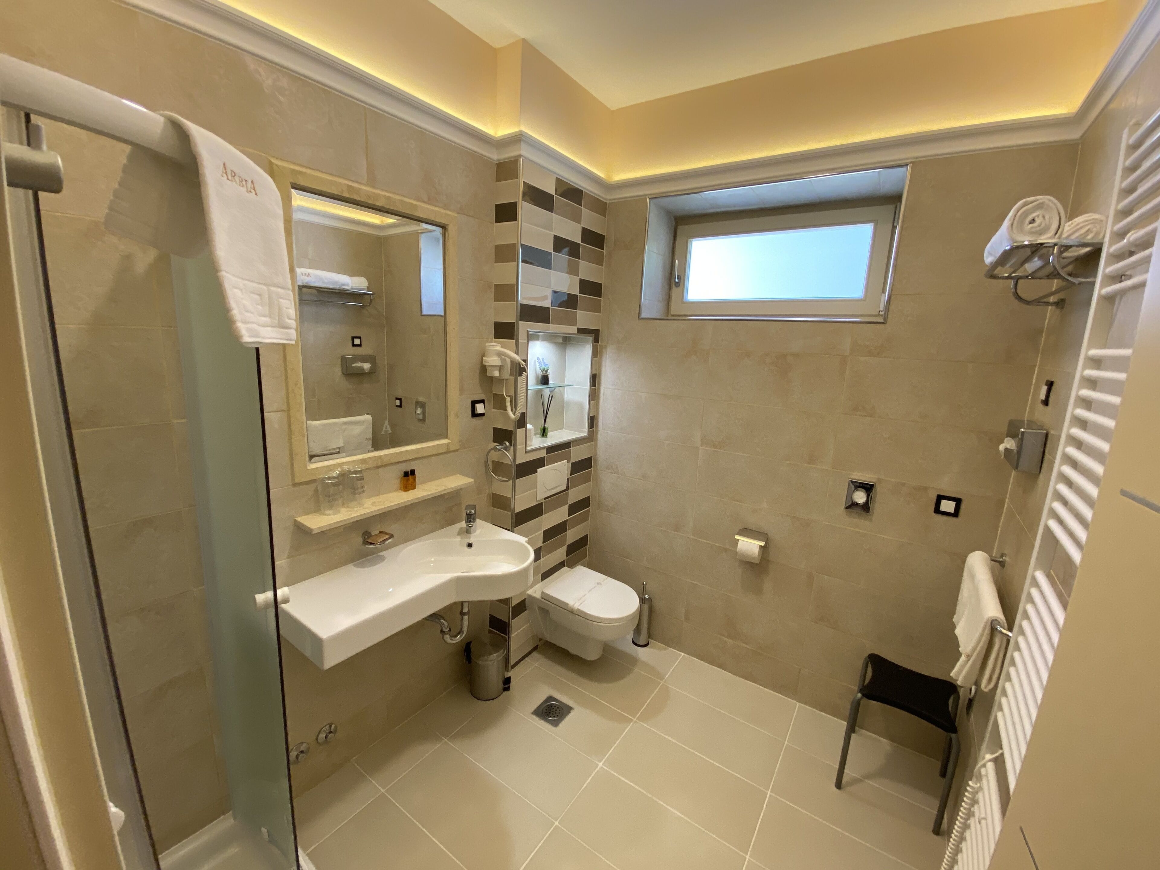 A modern bathroom with a glass shower enclosure, a vanity with a mirror, a toilet, and a small window.