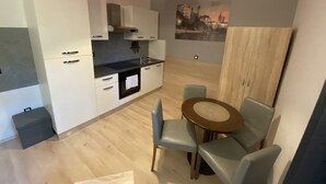 Una cocina moderna con armarios blancos, un horno negro y una lámpara colgante roja. Hay un comedor con una mesa redonda y cuatro sillas.