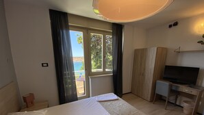 Habitación de hotel con una cama, un escritorio con televisor y vista al mar por la ventana.