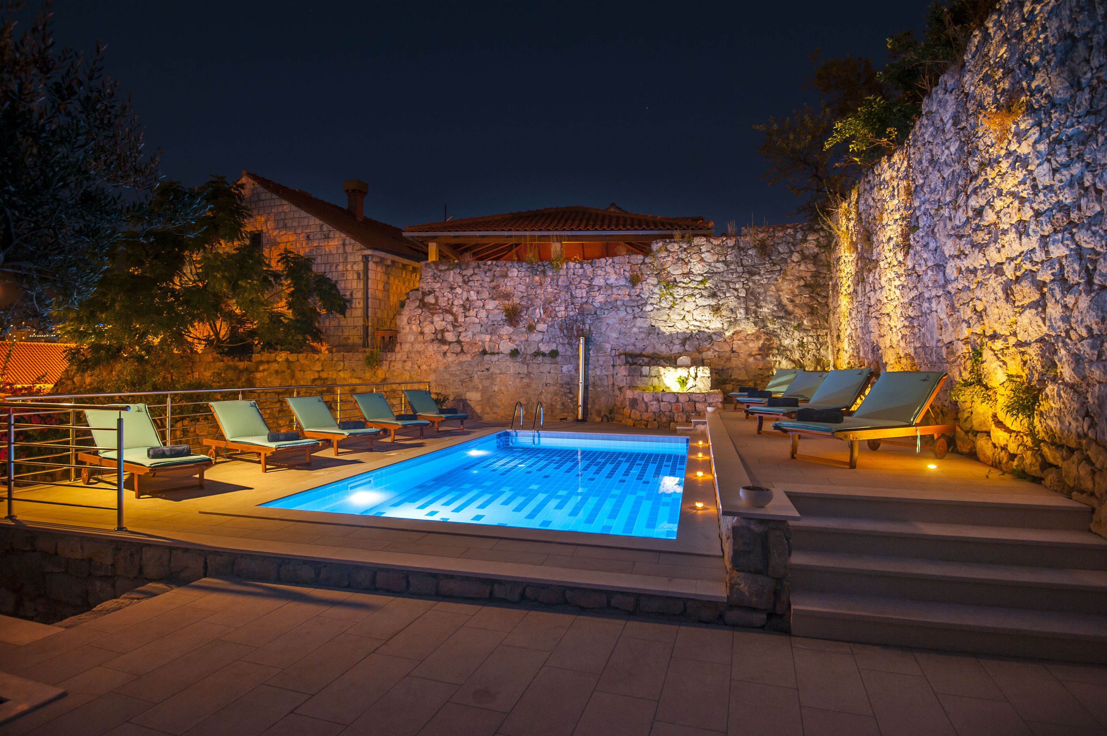 A swimming pool with lounge chairs and a stone wall.