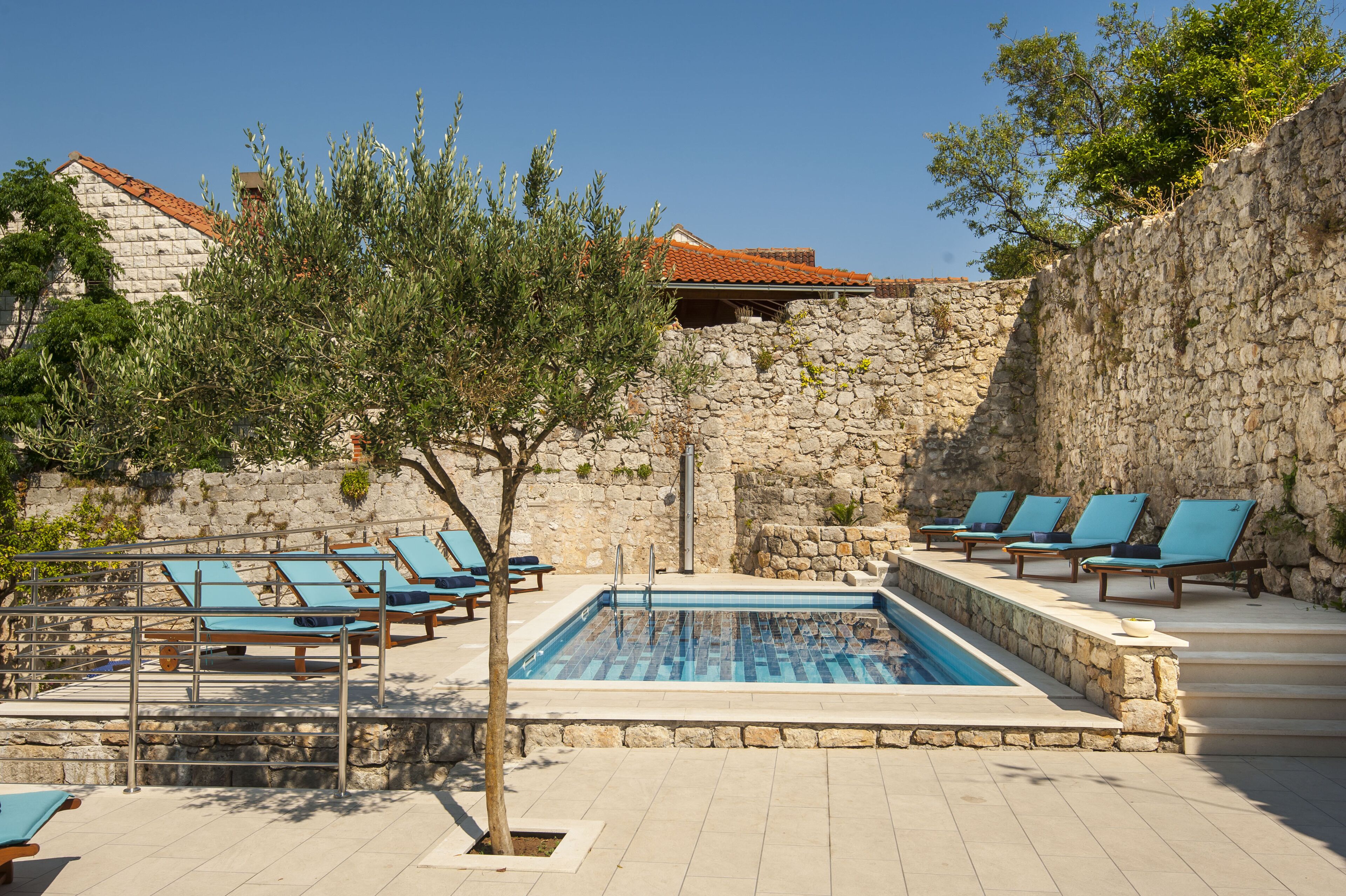 A swimming pool with lounge chairs, a stone wall, and a tree.