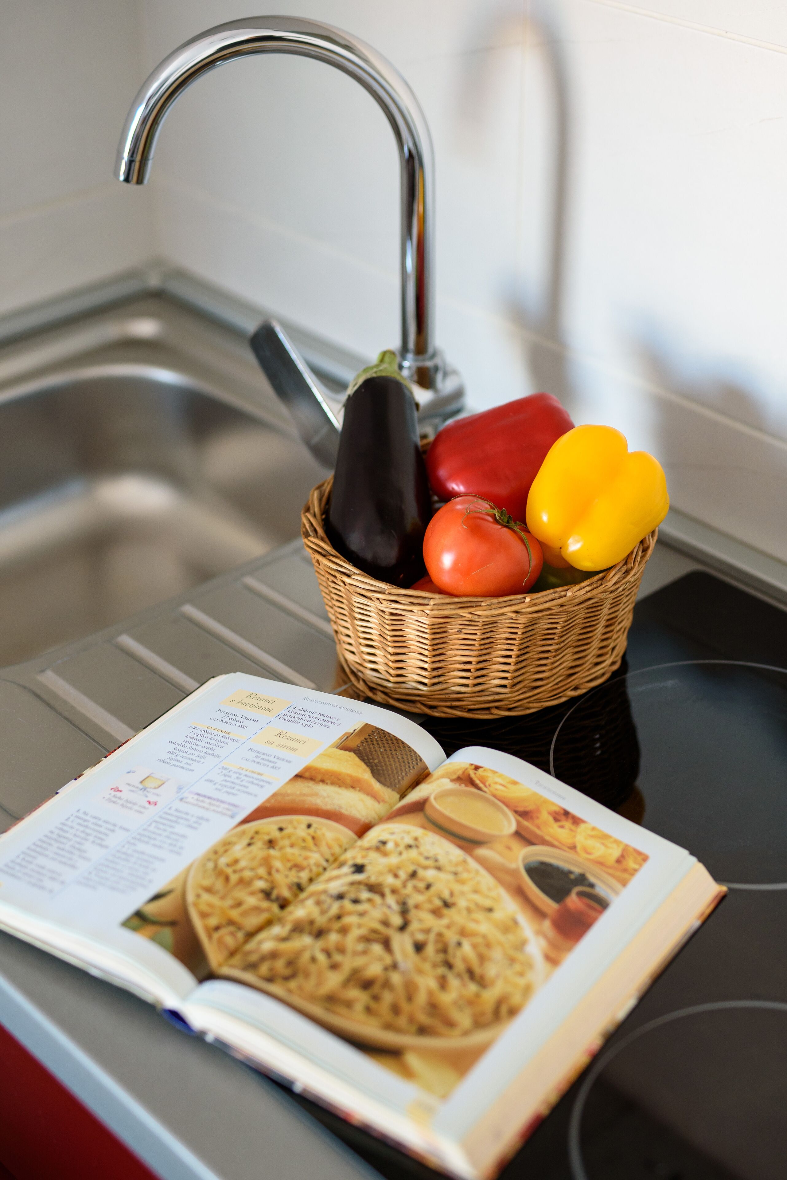 A kitchen counter with a basket containing vegetables and a cookbook.