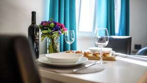 A dining table set with plates, glasses, a bottle, and a floral arrangement. - California Apartments II (Dubrovnik)