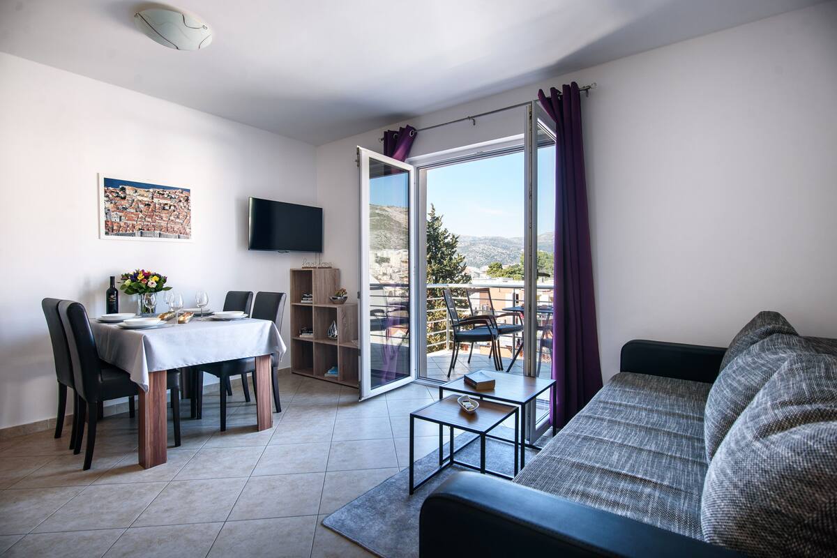 Un salon moderne comprenant un coin repas, un canapé, un téléviseur et une porte-fenêtre coulissante donnant sur un balcon.