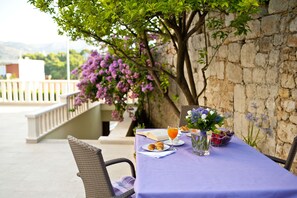 A table set outdoors with a book, croissants, a glass of orange juice, and a fruit bowl. - California Apartments II (Dubrovnik)