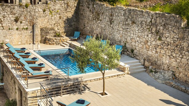A stone-walled pool area with lounge chairs and a tree. - California Apartments II (Dubrovnik)