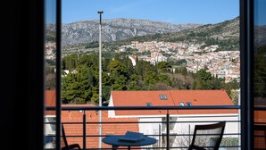 A balcony with a table and chairs, overlooking a town with red-roofed buildings and a mountain in the background. - California Apartments II (Dubrovnik)