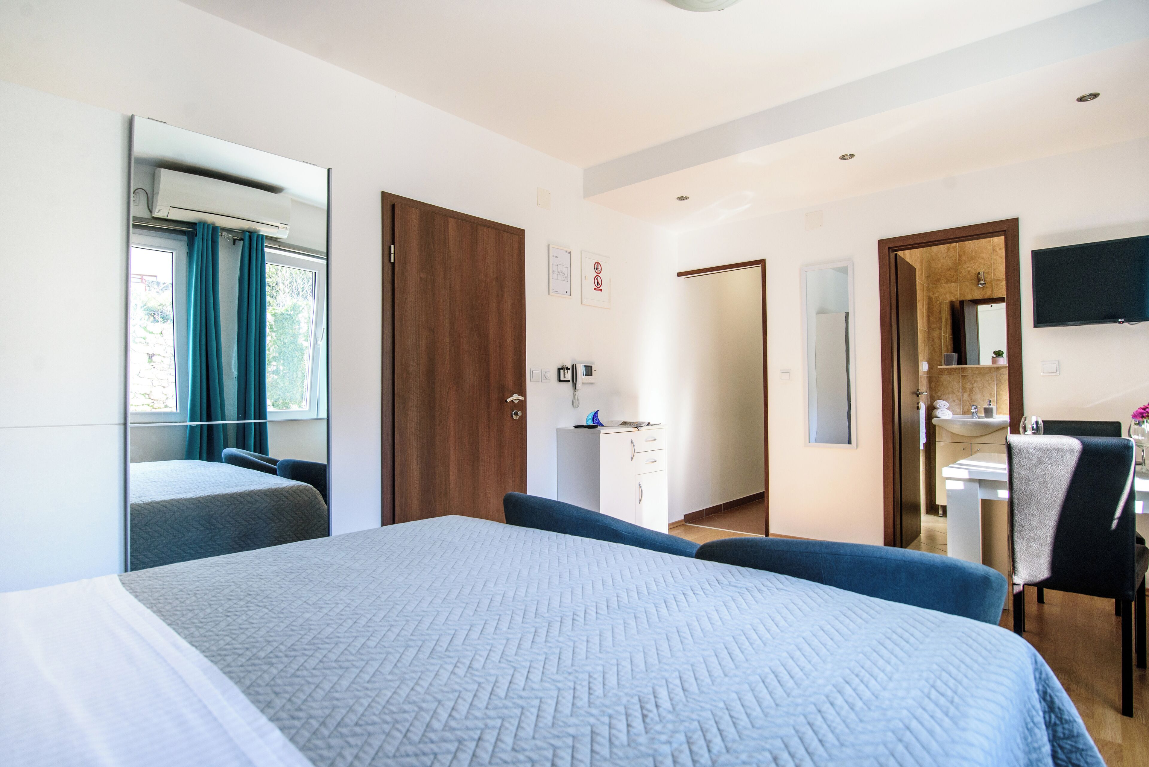 A hotel room with a large bed, a desk, a chair, a mirror, and a TV.