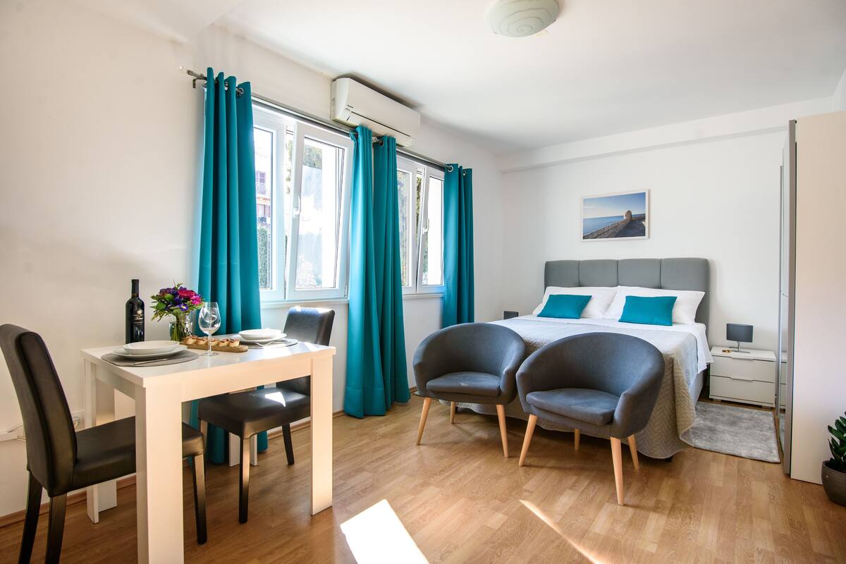 Une chambre moderne avec un lit, deux chaises, une table à manger et une fenêtre avec des rideaux.
