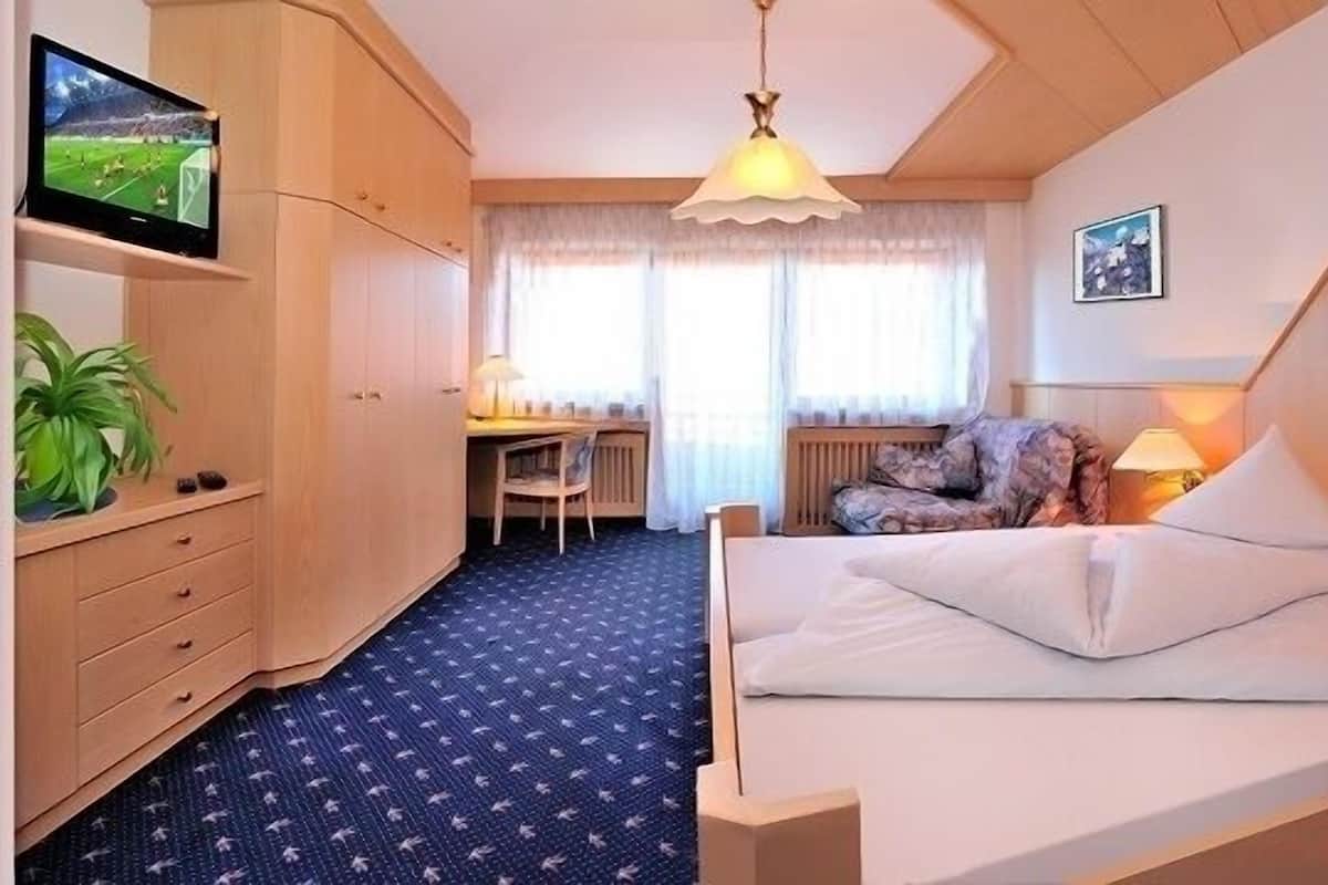 Ein Hotelzimmer mit Bett, Nachttisch, Lampe, Fernseher, Schreibtisch, Stuhl und einer Pflanze.