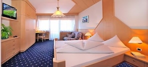 A hotel room with a bed, bedside table, lamp, TV, desk, chair, and a plant. - Hotel Hochrain (Naz Sciaves)