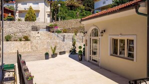 Un bâtiment doté d’une façade en pierre, d’un toit en tuiles et d’une petite cour intérieure agrémentée de plantes en pot et d’un banc.