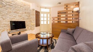 Un salon moderne avec un mur en pierre, un téléviseur à écran plat, des canapés gris et une cloison en bois.