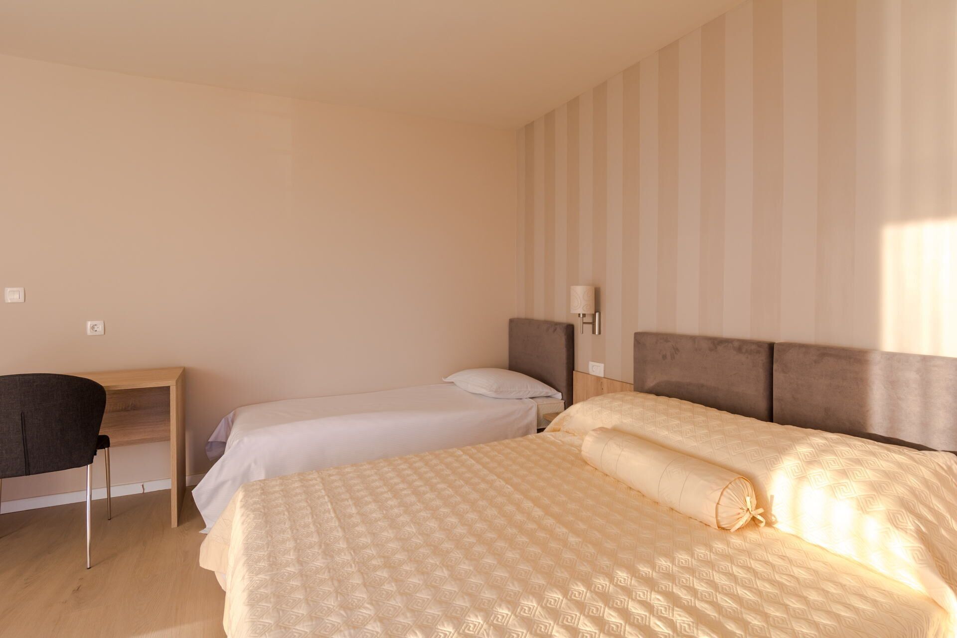 A hotel room with two single beds, a desk, and a chair.