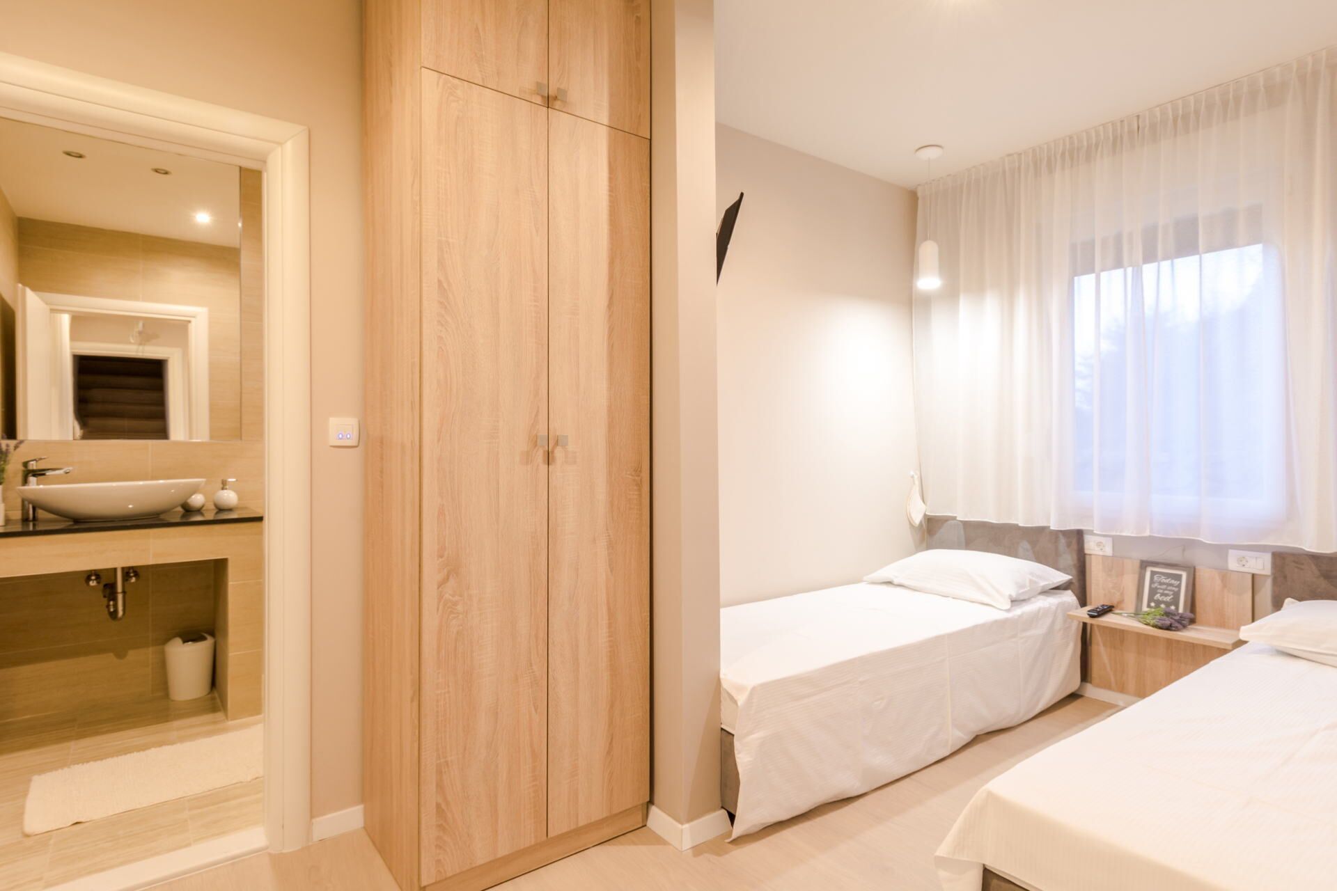 Un dormitorio con un armario de madera, una mesita de noche, una cama y una ventana con cortinas.