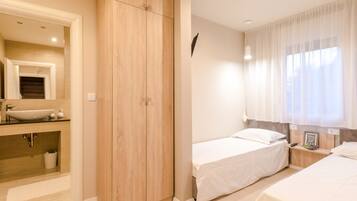 Un dormitorio con un armario de madera, una mesita de noche, una cama y una ventana con cortinas.