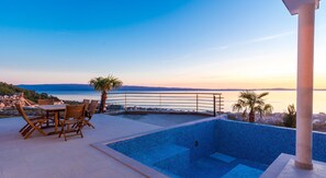 A pool area with a view of the sea and mountains, wooden furniture, and a palm tree. - Luxury Villa White Velvet with Pool (Podstrana)