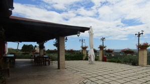 An outdoor patio with brick flooring, tables, chairs, and a covered area with hanging lights.