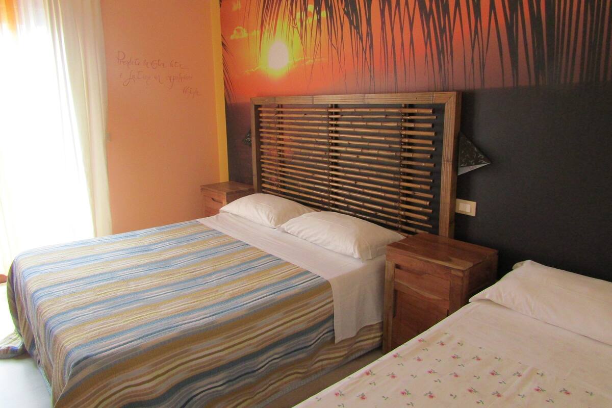 A double bed with a striped bedspread and a plain pillow, a wooden nightstand, and a headboard with horizontal slats.