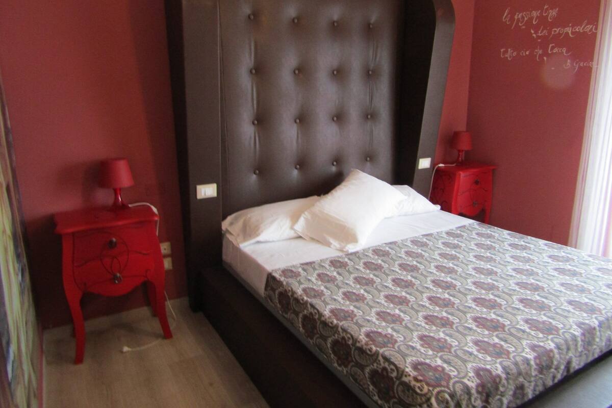 A bedroom with a large bed, a red nightstand, and a red dresser.