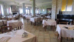 A spacious restaurant with multiple tables set for dining, a stone fireplace, and a television screen.