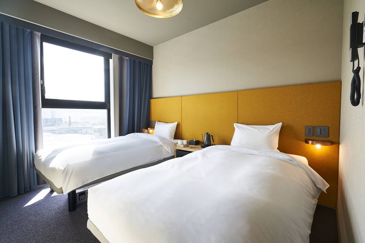 A hotel room with two beds, a city view, a coffee machine, and a phone on the wall.