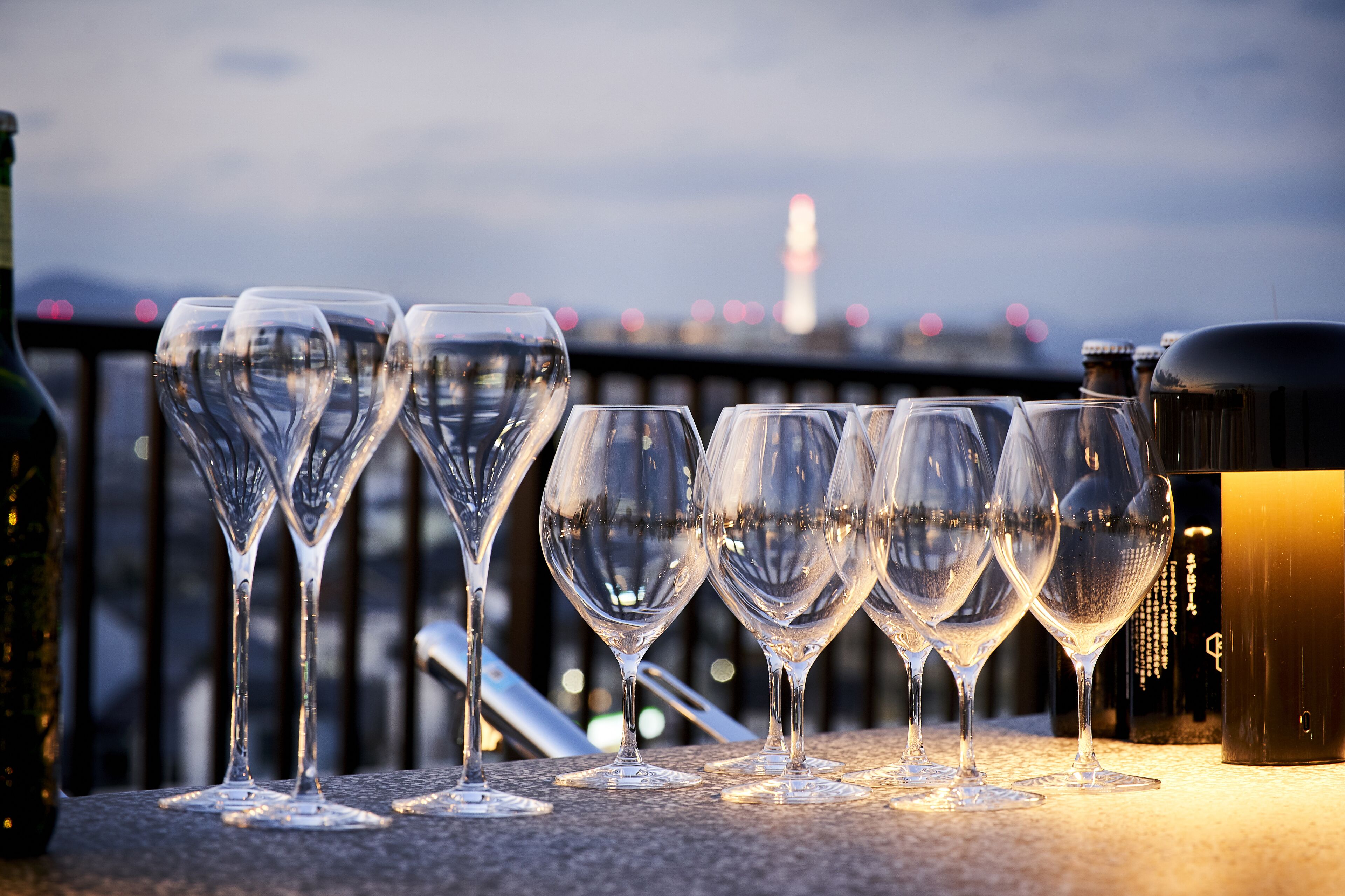 A row of empty wine glasses on a balcony with a cityscape and a tower in the background.