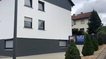 Un edificio moderno de dos pisos con fachada blanca y techo oscuro, que cuenta con numerosas ventanas y un camino de acceso pavimentado.