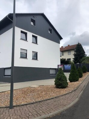 Ein modernes, zweistöckiges Gebäude mit weißer Fassade und dunklem Dach, ausgestattet mit zahlreichen Fenstern und einer gepflasterten Auffahrt.