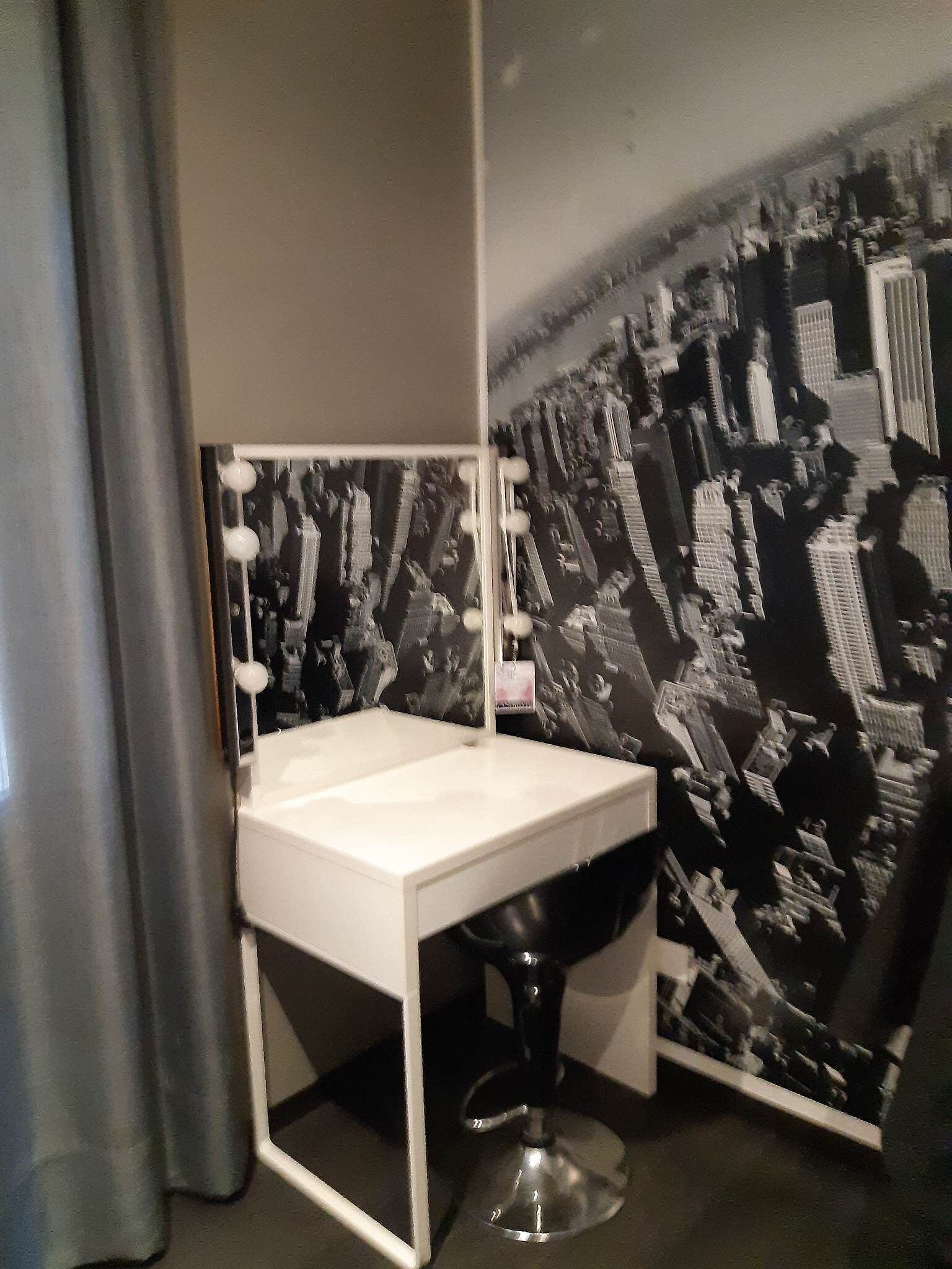 Een badkamer met een wastafel, spiegel en behang met een zwart-wit stadsgezicht.