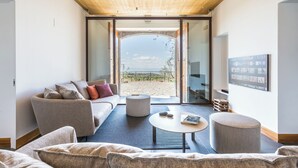 A modern living room with a sofa, a round table, and a view of the beach through large glass doors. - Snowshoe (Ragalna)
