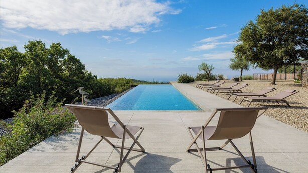 A pool area with lounge chairs, a clear blue pool, and a view of the sea. - Snowshoe (Ragalna)