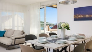 A modern dining area with a white table set for four, surrounded by beige chairs. A vase with flowers is on the table, and a cityscape painting is on the wall. - Luxury Villa Juliet with Heated Pool (Milna)