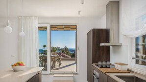 A modern kitchen with a view to the outdoors, a dining area with a table and chairs, and a large window with curtains. - Luxury Villa Juliet with Heated Pool (Milna)