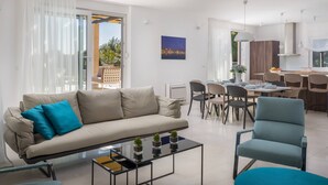 A modern living room with a sofa, coffee table, and chairs. A dining area with a table and chairs is visible in the background. - Luxury Villa Juliet with Heated Pool (Milna)